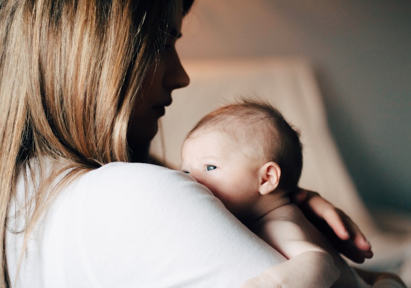 Una madre sostiene a su bebé recién nacido contra su hombro, en luz cálida